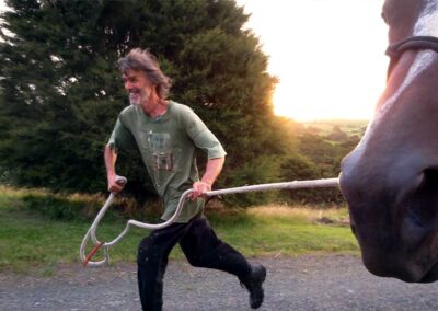 middle-aged man with beard, olive green t-shirt and black pants running enthusiastically with a horse on a white lead-rope towards the left, only the tip of the horse's nose showing in right corner of image