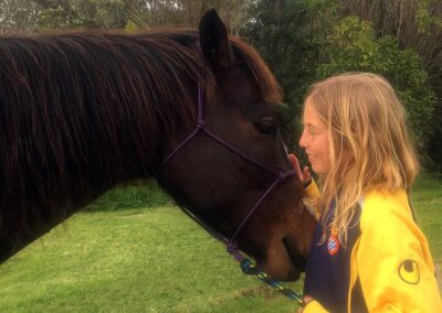 dark brown horse with fluffy hair and smiling blond girl in yellow sports top nose to nose