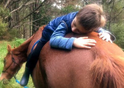 lttle boy in blue clothes lying on his tummy front to back on the back of a chestnut horse
